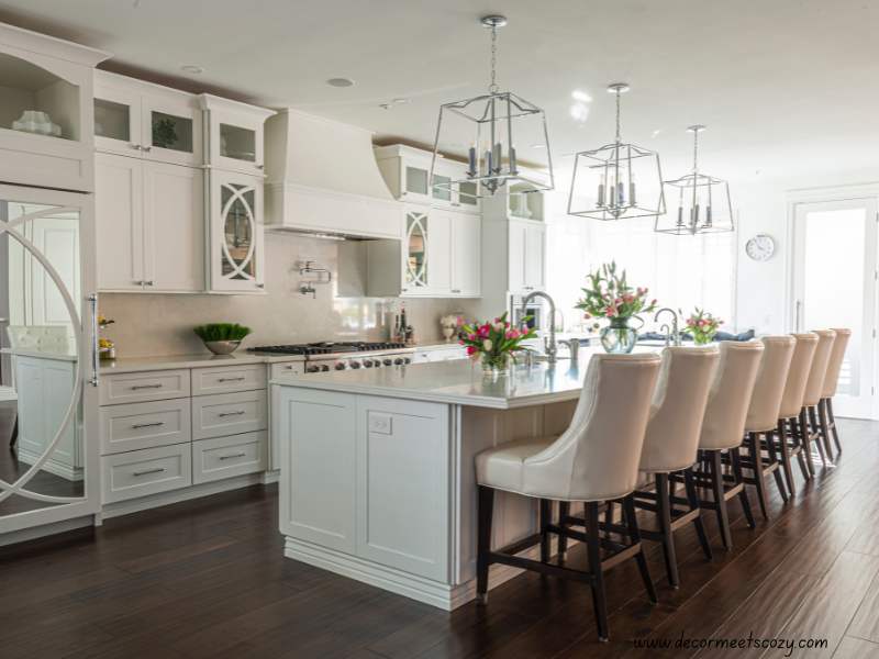 The-image-shows-a-white-coloured-kitchen-with-chairs-neatley-placed-and-styled-there-is-also-3-pendant-lights